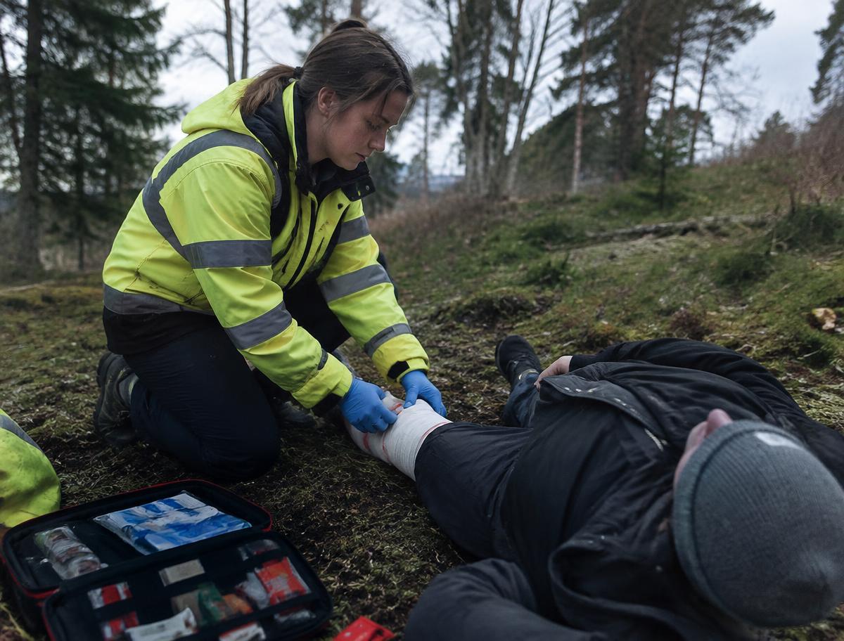 Outdoor first aider bandaging a casualty's leg in woodland